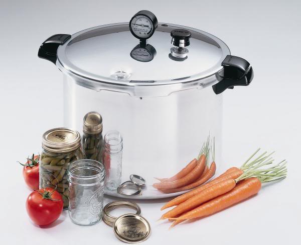 Pressure canner surrounded by carrots, tomatoes and herb jars.