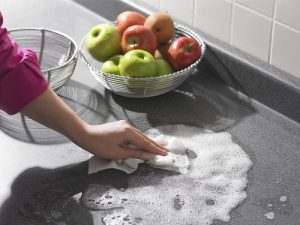 a hand washing a counter with a bowl of apples nearby