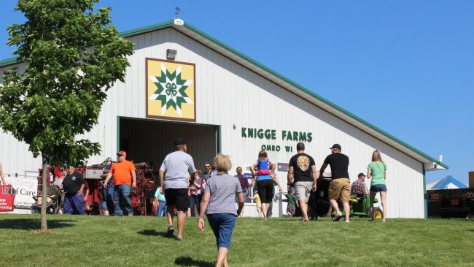 People gathered in front of a barn with the 4-H Clover over the door.