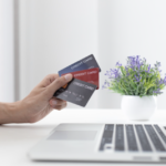 Image of person holding 3 credit cards in front of a laptop.