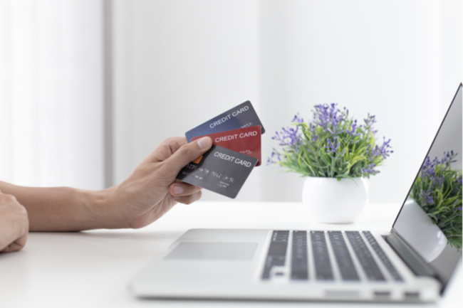 Image of person holding 3 credit cards in front of a laptop.