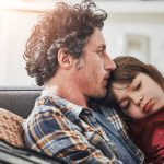 Photo of a father holding his daughter while sitting together on a couch.