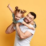 father playing with daughter, holding her on his shoulder like an airplane.