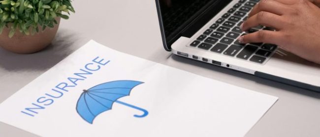 Image of paper with the word insurance and an umbrella printed on it, next to a laptop with someone's hand typing