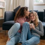 mother kissing head of teen daughter while sitting next to each other